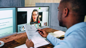 videobewerking door iemand (deels in beeld) die een document met tekst vasthoudt en op achtergrond twee beeldschermen
