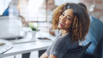 dame gezeten aan bureau kijkt lachend over haar schouder naar achteren